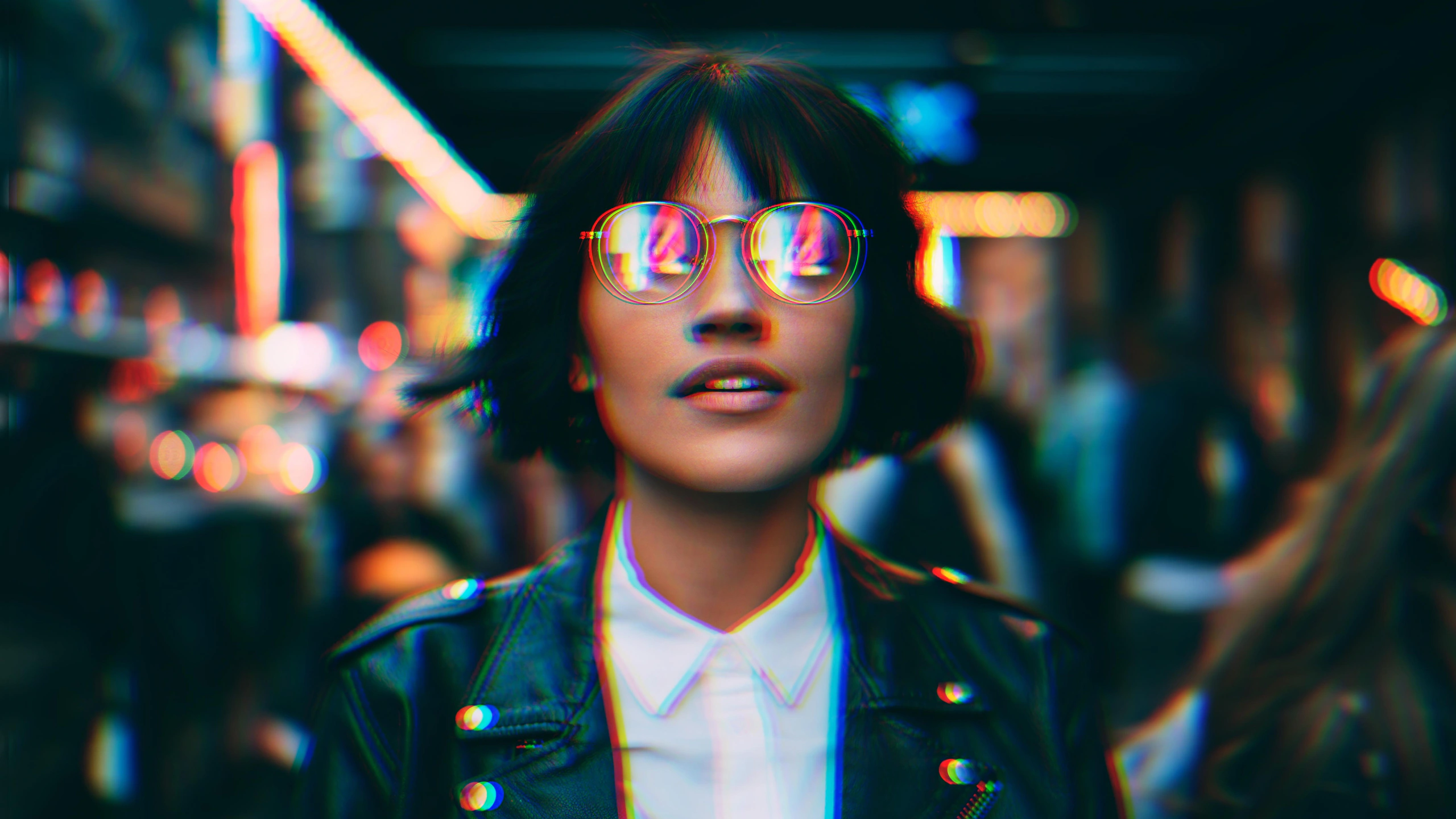 Ragazza con caschetto nero e occhiali rotondi che riflettono luci al neon, giacca di pelle e camicia bianca, in una strada notturna sfocata, con colori sdoppiati in rosso, verde e blu